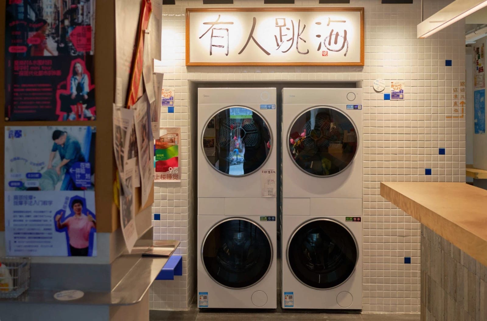 Shared washer-dryers for guests at Tiaohai Living, below a framed 有人跳海 sign